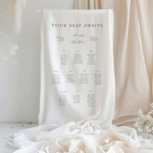 fabric seating chart sign for a wedding event, white linen fabric with black text that says "your seat awaits" and then the various tables with the guest names below